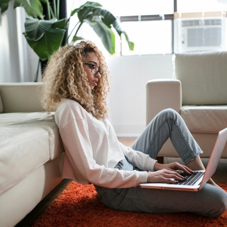 Frau mit lockigen Haaren sitzt am Boden und arbeitet am Laptop. Frau mit lockigen Haaren sitzt am Boden und arbeitet am Laptop.