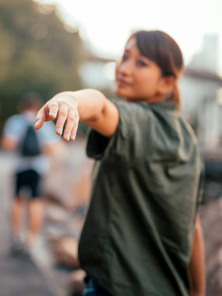Frau in grüner Jacke, die mit ausgestrecktem Arm in die Kamera zeigt. Unschärfe im Hintergrund. Frau in grüner Jacke, die mit ausgestrecktem Arm in die Kamera zeigt. Unschärfe im Hintergrund.