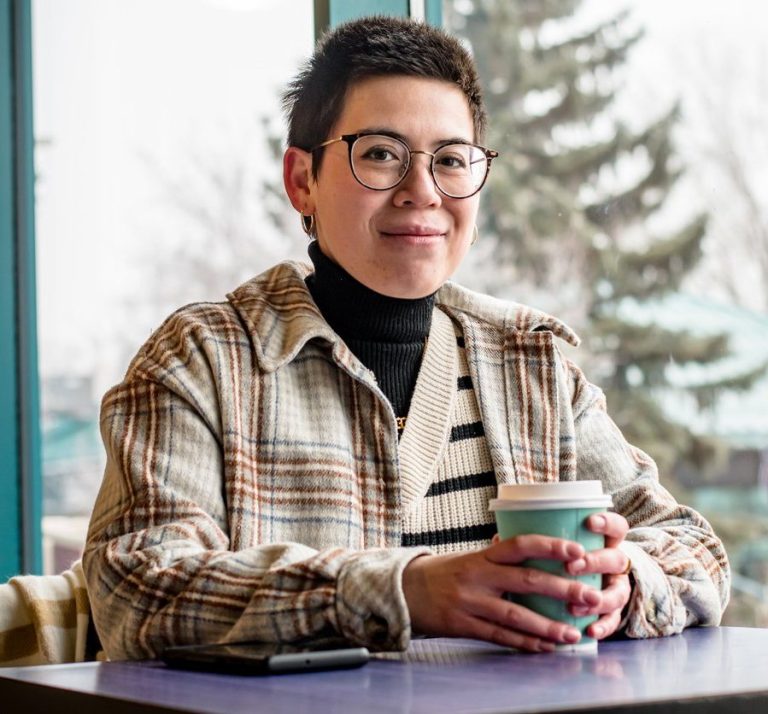 Junge autistische Person mit Brille, die an einem Tisch sitzt und eine Tasse Kaffee hält. Junge Person mit Brille, die an einem Tisch sitzt und eine Tasse Kaffee hält.