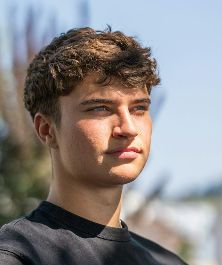 Junger Mann mit dunklem Haar, trägt ein schwarzes Shirt und schaut nachdenklich in die Ferne.